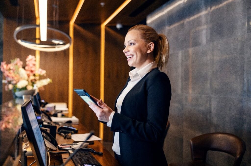 Eine glückliche Rezeptionistin unterhält sich mit einem Hotelgast und macht ein