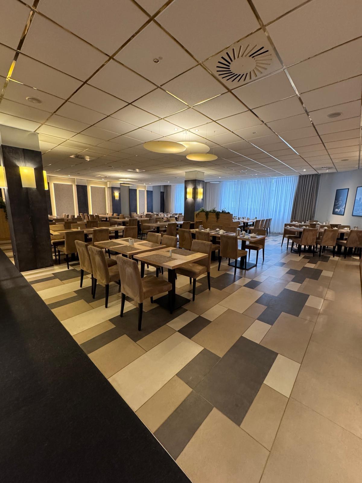 Ein leerer Speisesaal mit modernen Holztischen und beige gepolsterten Stühlen