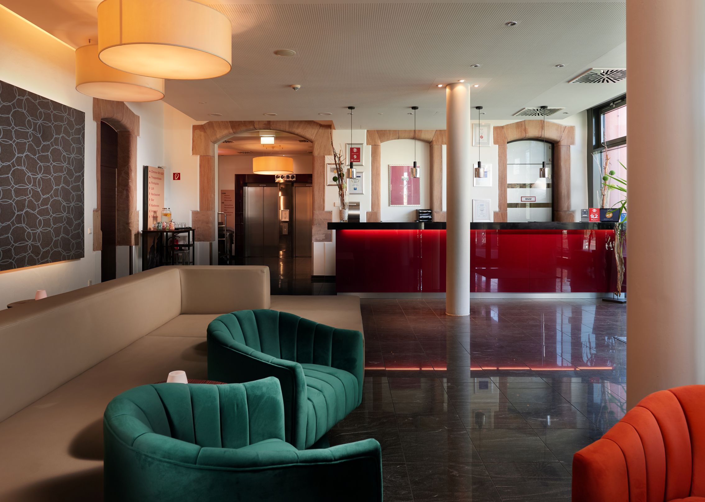 Helle Hotellobby mit roten Tresen und grünen Sesseln, ruhig und modern